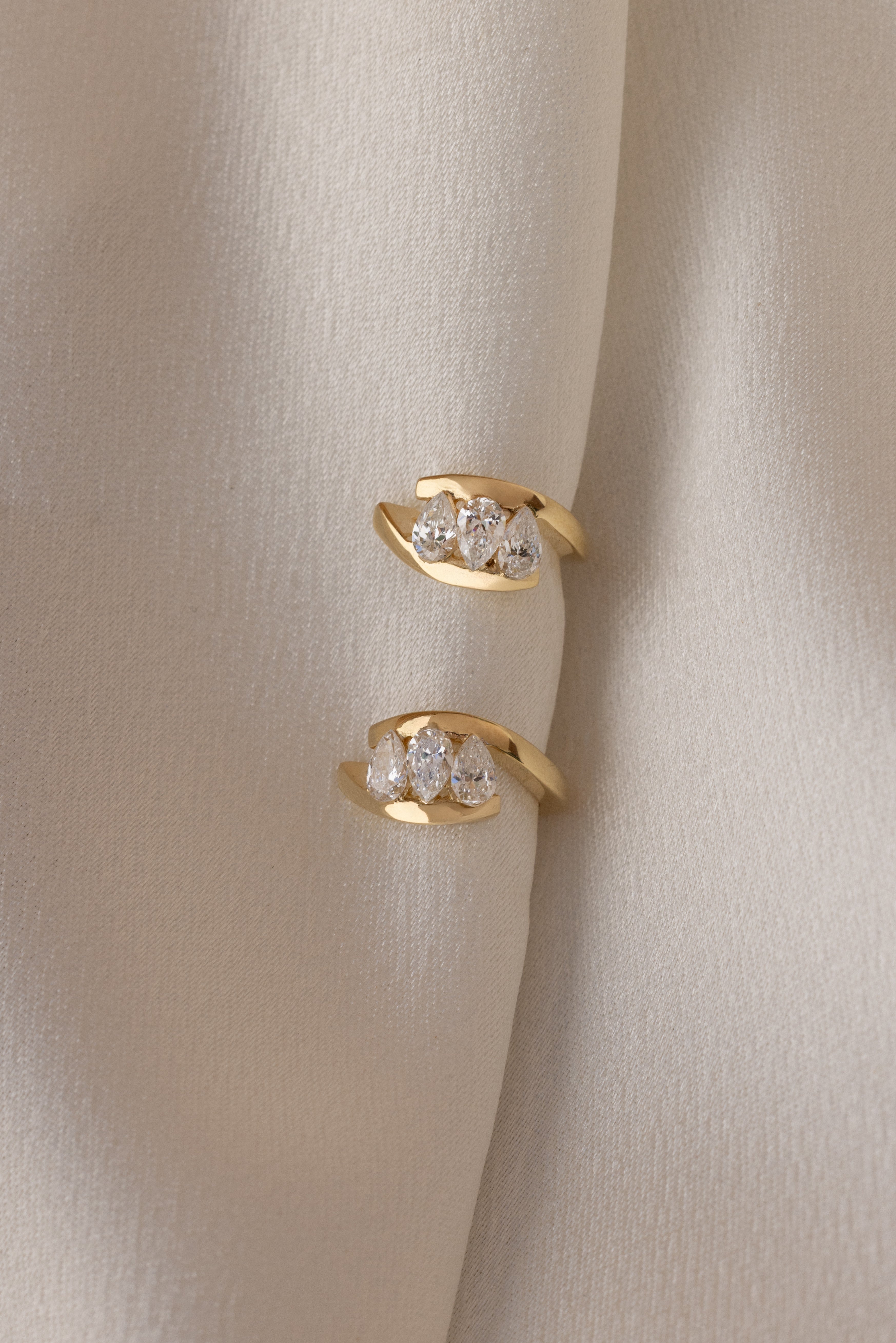 pair of 18k yellow gold pear triplet hoops on cream fabric